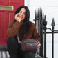 Woman holding a brown handbag in front of a red door