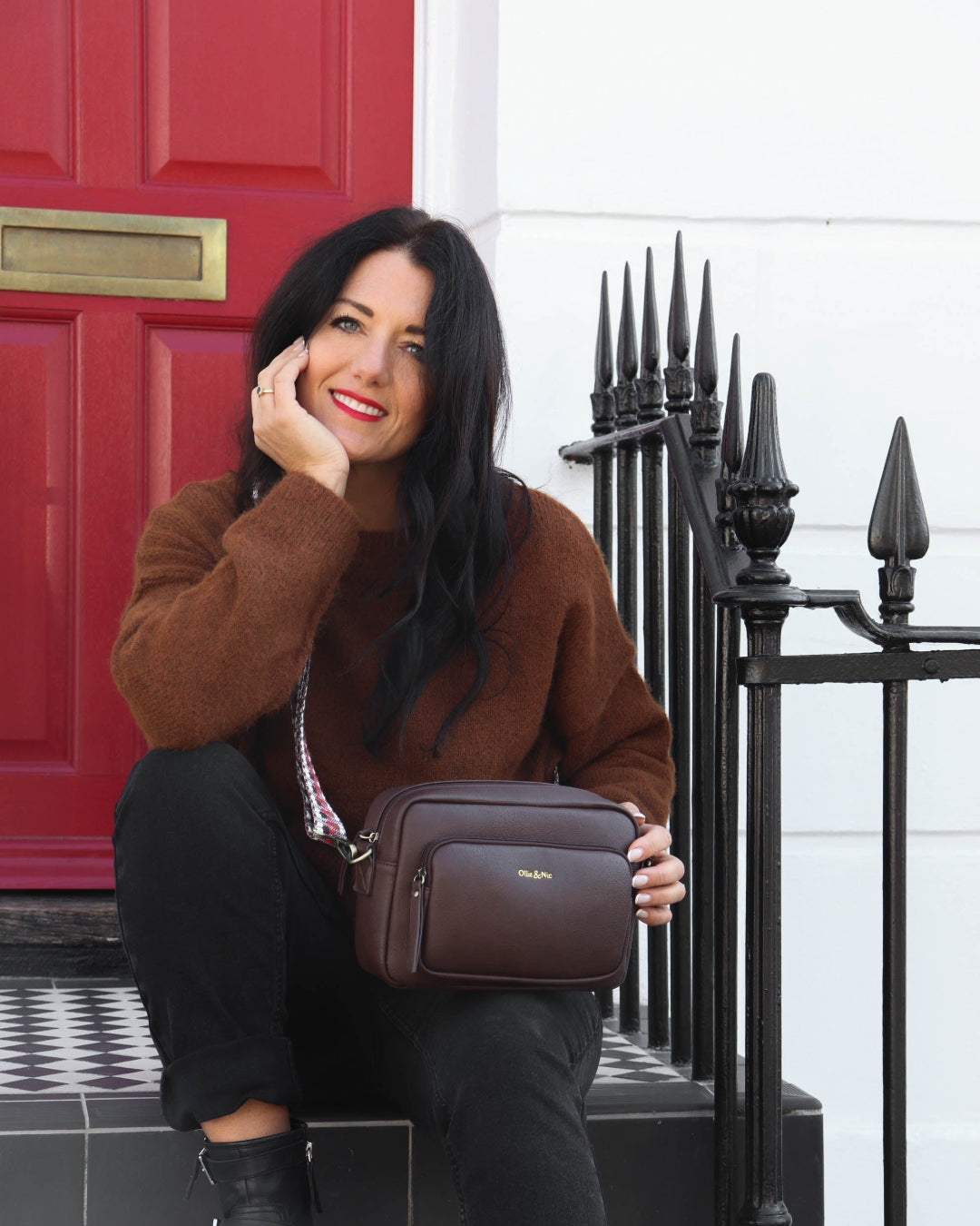 Woman holding a brown handbag in front of a red door