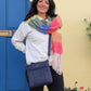 Woman wearing a colorful scarf and blue bag standing in front of a blue door and yellow wall.