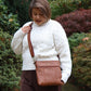 Woman wearing a white sweater and brown pants with a brown Eddie bag outdoors.