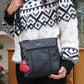 Person wearing a black and white patterned sweater holding a black Eddie Crossbody with a red heart charm.